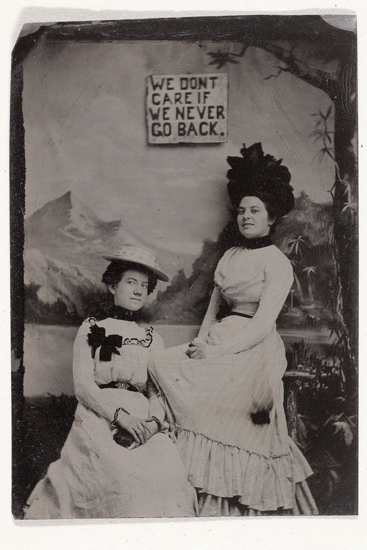 Portrait of two women, standing and sitting in front of a painted background canvas and the text 'WE DON'T CARE IF WE NEVER GO BACK' - anonymous artist, c. 1895 - 1910
