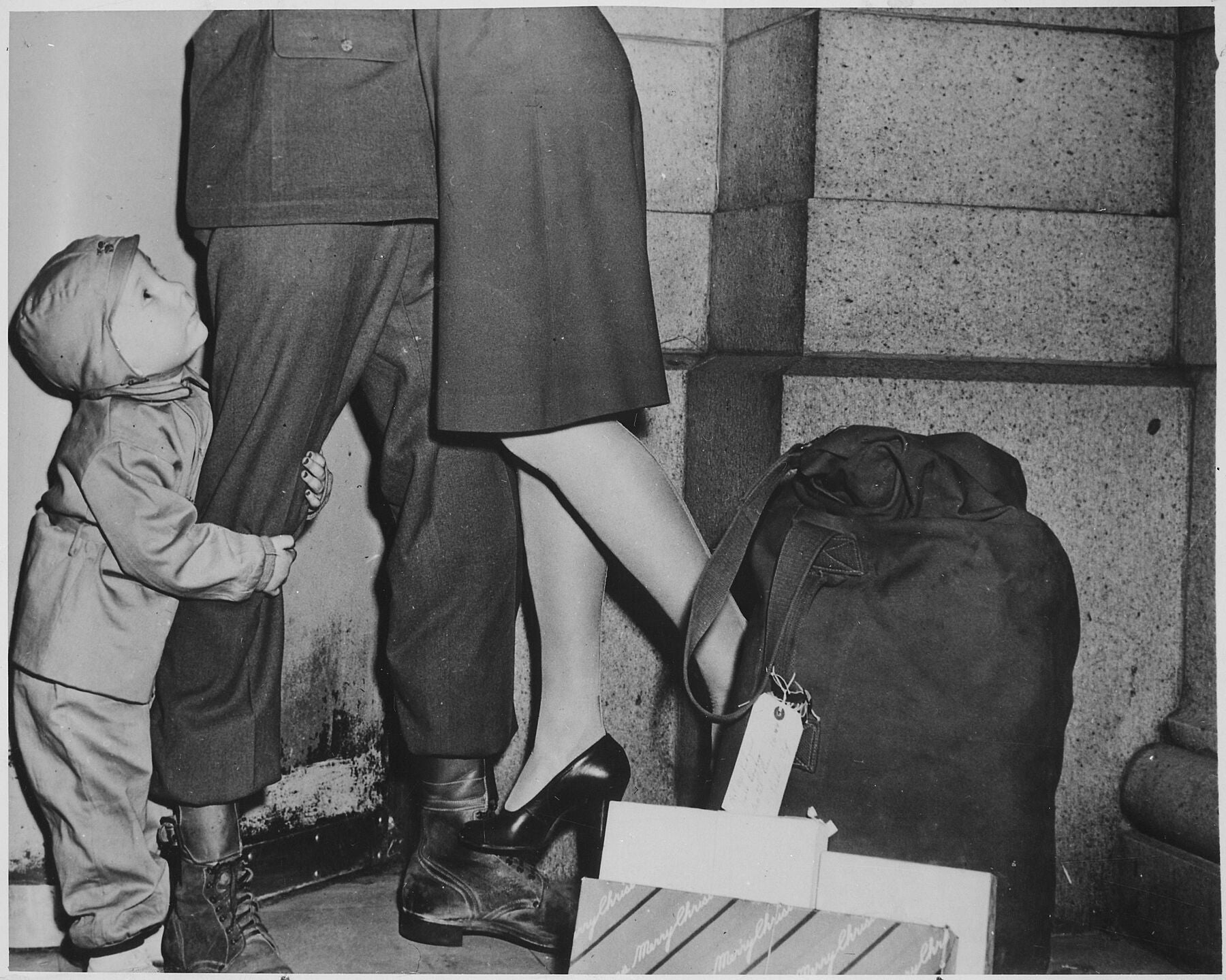 A youngster, clutching his soldier father, gazes upward while the latter lifts his wife from the ground to wish her a Merry Christmas Overseas Operations Branch New York Office. News and Features Bureau - 12_1944