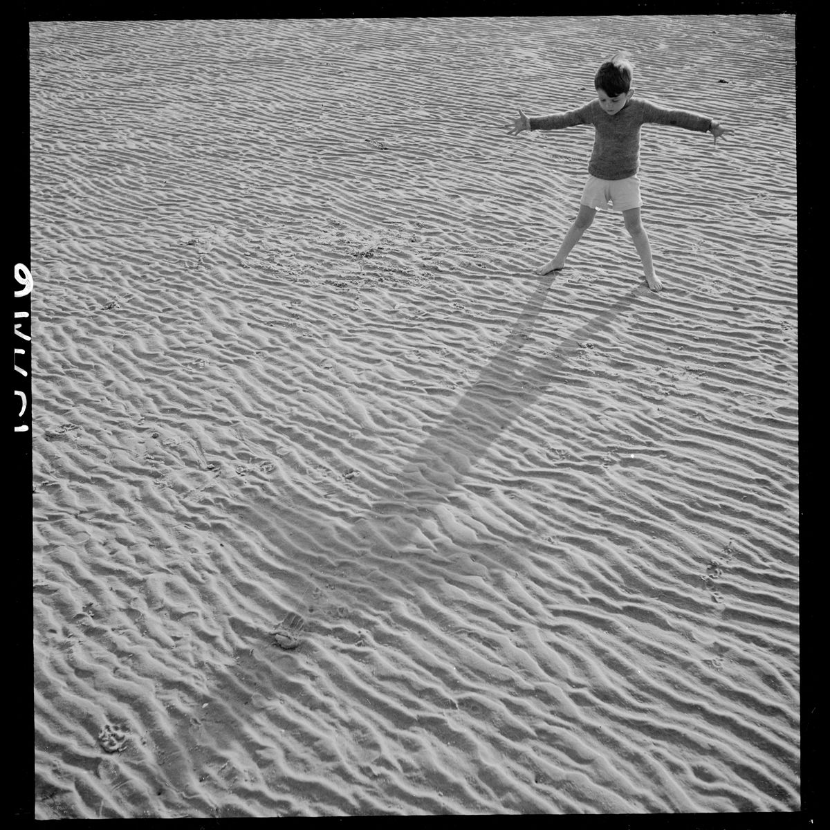 A boy standing on a beach looking at his shadow by Toni Frissell - 1944