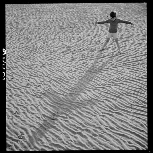A boy standing on a beach looking at his shadow by Toni Frissell - 1944