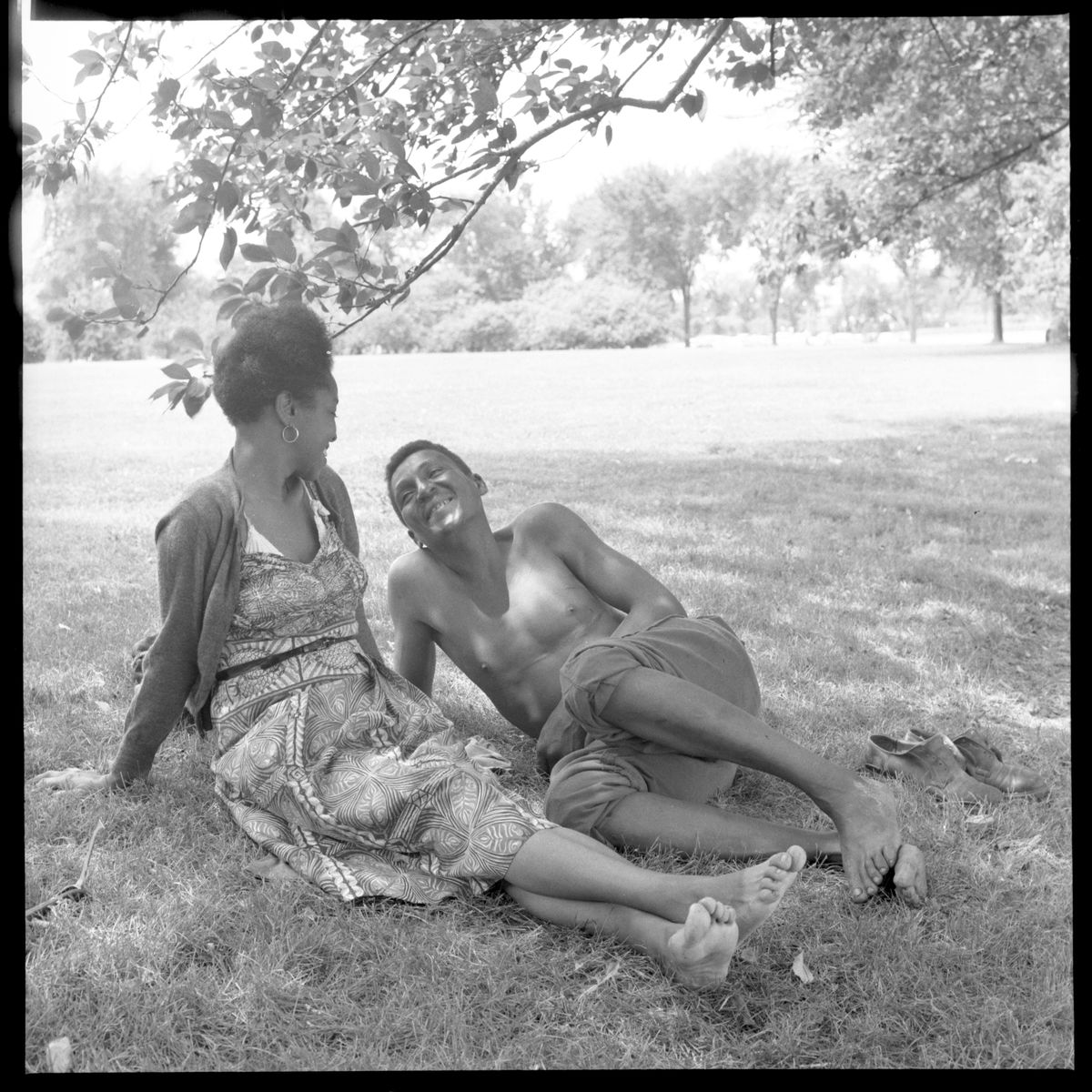 Woman and man seated on grass near trees by Toni Frissell - c.1955